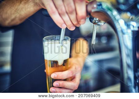 Close-up of young bartender pouring beer while standing at the bar counter.