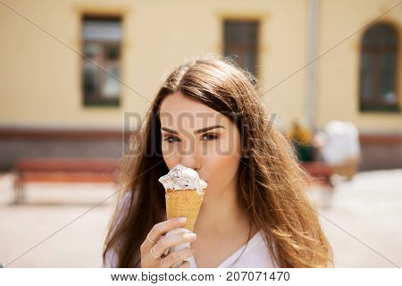 Young cheerful girl is eating ice cream on walk, on promanade.
