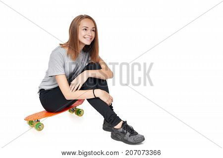 Teen girl in full length sitting on skate board smiling looking up at blank copy space, isolated on white background