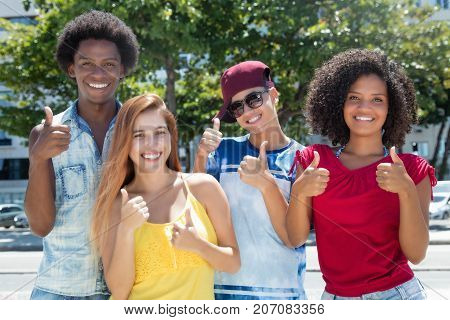 Multi ethnic group of latin and african american and caucasian young adults showing thumb outdoor in the summer in the city