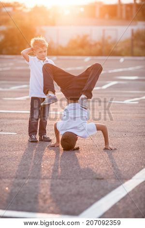 The boy is showing a headstand on the street. Younger brother admires his brother