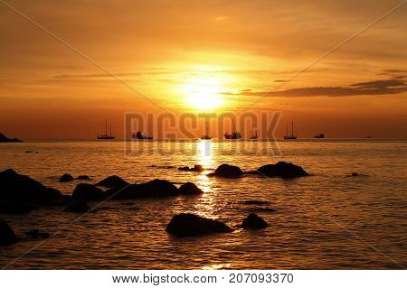 Golden sunset at beach island Sunset over the beach with rocks in the foreground Boats and yachts in the distance
