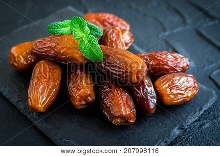Dried date and green mint on black stone background. Heap of dates close up. Healthy snack.