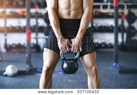Unrecognizable young fit man in modern gym doing kettlebell swings. Close up.