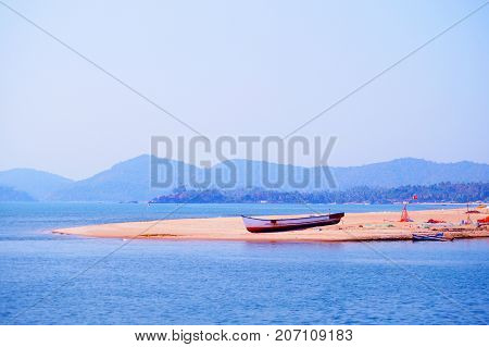 Lonely fisherman boat on the coast near Palolem beach. Talpona river. Mountain on the background.