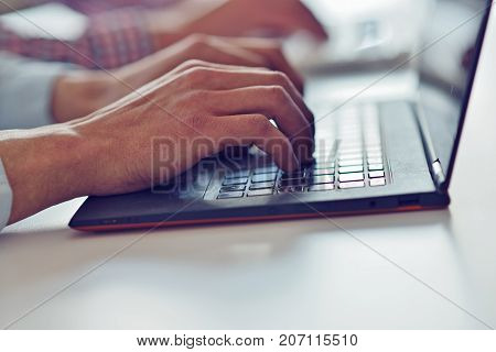 Man's hands typing on laptop keyboard in office