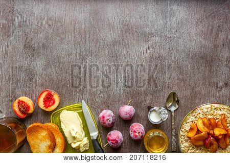 Oatmeal with plums and peach, toast with butter and honey on a wooden table. A cup of black tea. The concept of a healthy breakfast. Top view. Copy space. Still life. Flat lay