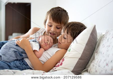 Two children toddler and his big brother hugging and kissing their newborn baby brother at home few days after delivery