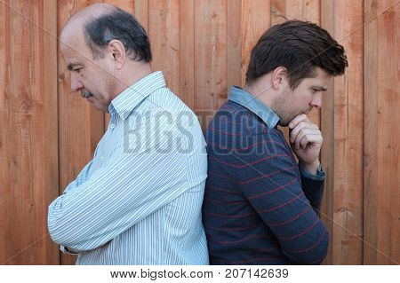 Portrait of quarreled elderly father and son. They stand spine to spine and do not want to speak to each other