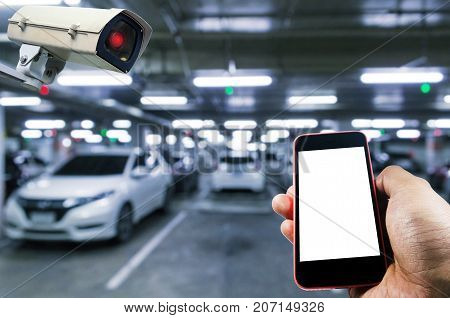 hand using smart phone monitoring and CCTV security indoor camera system operating in indoor car parking garage area RFID solution management system internet security and safety technology concept