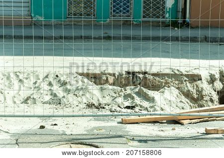 Metal safety fence on the street parallel with the trench full of sand after road exscavation work
