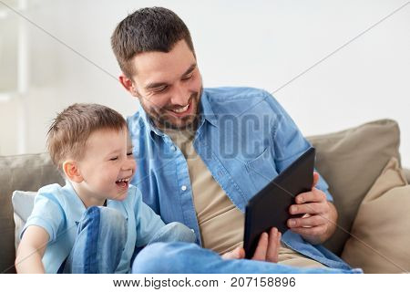 family, fatherhood, technology and people concept - happy father and little son with tablet pc computer sitting on sofa at home