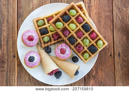 Belgian waffels, cupcakes and ice cream cone with grape, blueberry, raspberry on wooden background