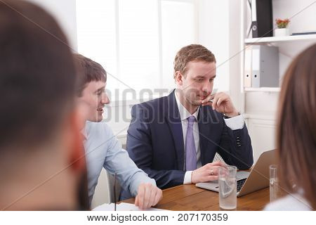 Business team meeting. Young successful emploee in official suit reading report at laptop. White office interior