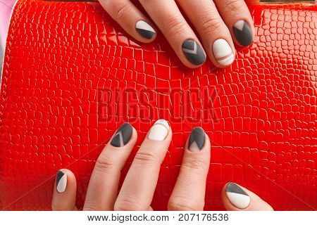 Elegant red ladies handbag in female hands. Trendy matte manicure and leather purse close up. Womans beauty and style.