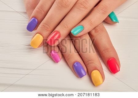 Multicolored manicure close up. Young woman hands with pastel manicure on white wooden background. Summer fashion manicure.