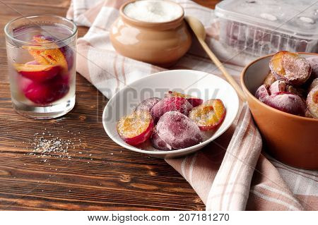 Still Life Of Plums Frozen On The Plate, In The Glass. Wooden Table, Rustic Table Cloth.