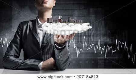 Cropped image of businessman in suit presenting in his hand modern city block with business sketches on background. 3D rendering.