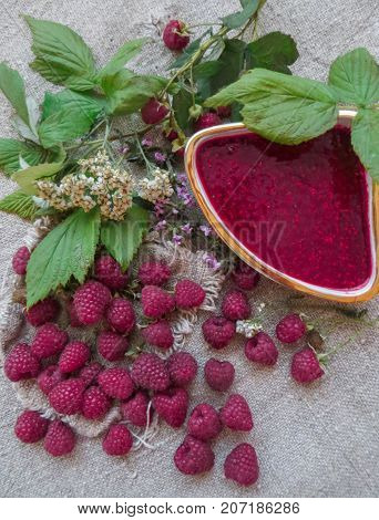 scattered on the table ripe fresh berries of raspberries along with jam.