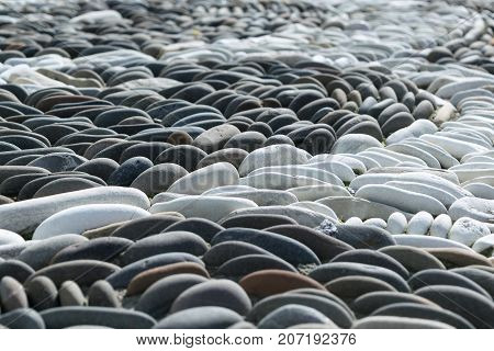 River or marine oval smooth stones or pebbles inlaid pattern. Pebble grey and white. Pattern in the form of an arc or semicircle. Day exposed to sunlight.