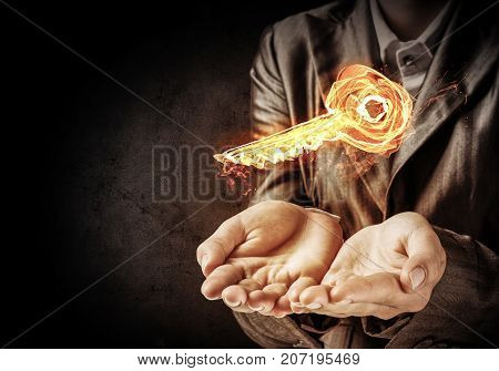 Closeup of businessman in black suit keeping flaming key symbol in hands with dark wall on background.