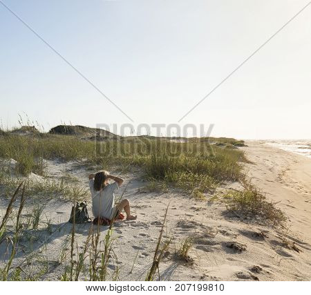 Seated woman in pristine sand dunes at Florida Gulf Coast beach looks out to sea as the sun rises.