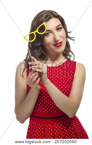 Youth Lifestyle Concept. Portrait of Sensual Alluring Caucasian Female Holding Yellow Artistic Spectacles Above Her Face. Posing In Red Polka Dot Dress Against Pure White.Vertical Image