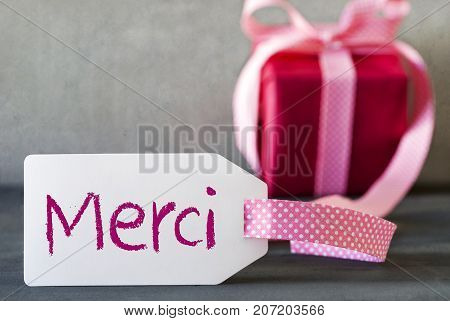 Label With French Text Merci Means Thank You. Pink Gift Or Present With Gray Cement Background