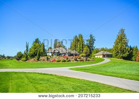 Asphalt road junction flowing over green lawn with big farmer's house on hill