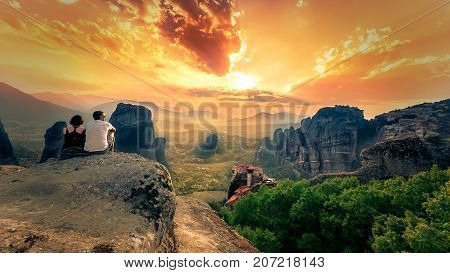 Couple enjoy the breathtaking view of Meteora Roussanou Monastery at sunset, Greece. Geological formations of big rocks with Monasteries  on top of them, on July 20, 2017.