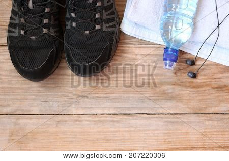 Sport equipment shoes water earphone and towel on wooden background