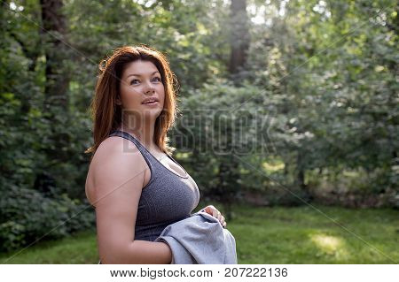 Young chubby pretty woman standing in forest in sunny day.