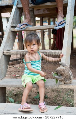 Boca de valeria Brazil - December 03 2015: child feeding sloth with green leaves on wooden stairs. Poverty and childhood concept. Human and wildlife