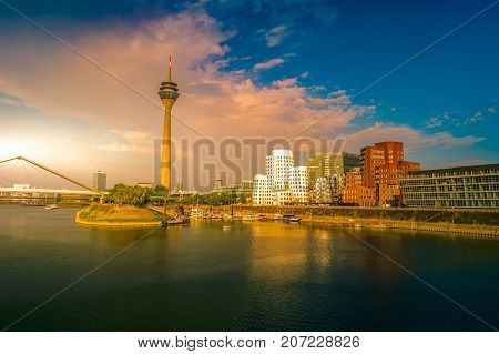 Looking at Media Harbor at Rhine-River in Dusseldorf in Germany. Media Harbor with Rhine-Tower and famous buildings in dramatic sunset light with their reflection in the water. Beautiful and colorful cityscape of the german city