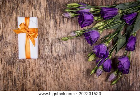 White gift box on a woody background and a bouquet of purple flowers. Delicate flowers are eustoma.