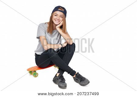 Teen girl in full length sitting on skate board smiling at camera, isolated on white background