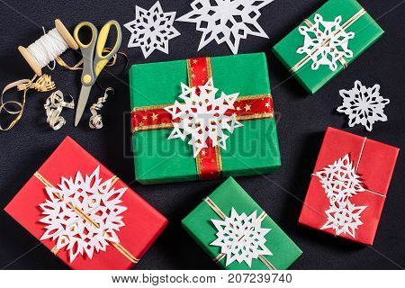 Decoration of gift boxes for Christmas with your own hands. DIY hobby. Boxes are wrapped in red and green paper tied with ribbons with handmade snowflakes. Original gift decoration