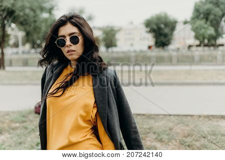 Portrait Of Stylish Modern Young Curly Woman In Coat Sunglasses. She On The Street And Looks Happy.