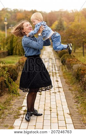 Happy joyful mother having fun throws up in the air child in autumn park