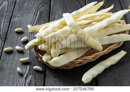 White string beans on wicker tray. Long white pods and seed beans on dark wooden table. New harvest. Ingredient in healthy and dietary food