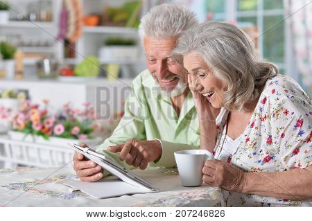 Happy senior couple using digital tablet in kitchen