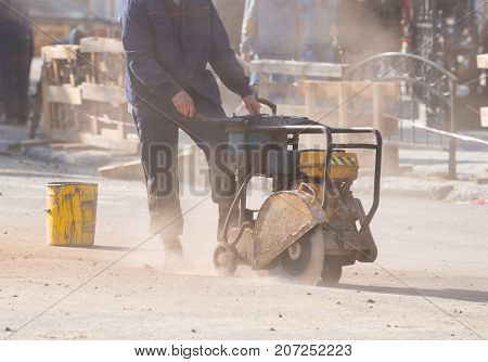 Worker cutting concrete road with diamond saw blade machine. Road reconstruction