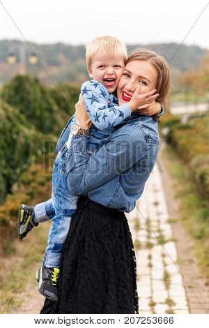 Happy joyful mother having fun throws up in the air child in autumn park