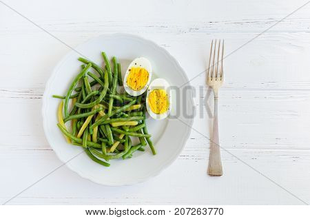 Cooked green beans with boiled eggs in white plate. Healthy vegetarian food concept. Top view.
