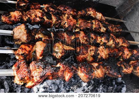 closeup of some meat skewers being grilled in a barbecue. side view