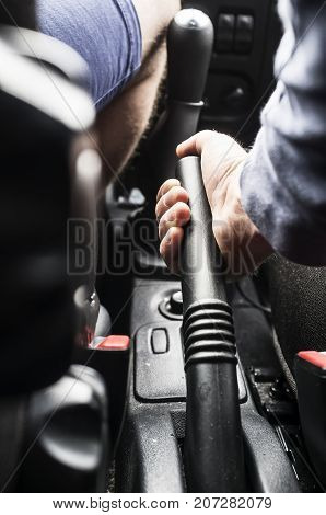 The man - driver holds the handbrake in the car. Close-up.