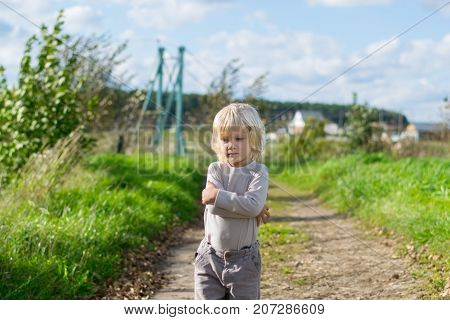 Seriouse blond boy staying embraced himself with his arms, country road to the Urals village