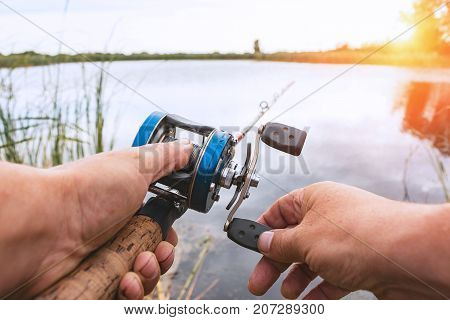 A man is fishing with a backcasting reel. Hands, a rod and a backcasting reel in the background of the rising sun