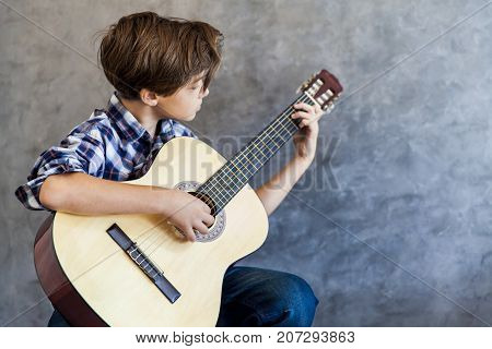 Cute teenage boy with acoustic guitar by the wall