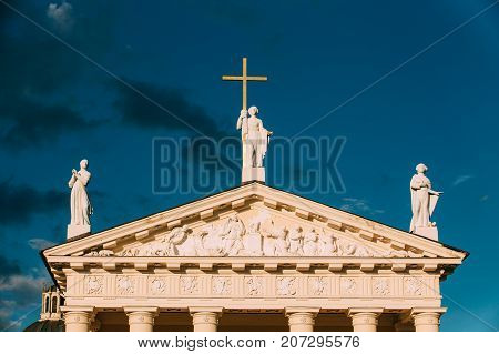 Vilnius Lithuania. Close Pediment Of Cathedral Basilica Of St. Stanislaus, St. Vladislav With Three Statues - St. Elena With Cross, St. Stanislaus, St. Casimir, Relief Sculpture Decoration, Blue Sky